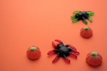 Sweet jelly candies in the form of huge black spiders with green and red legs and pumpkins on a bright orange background. Copy space. Sweet Helloween. Trick or treat concept