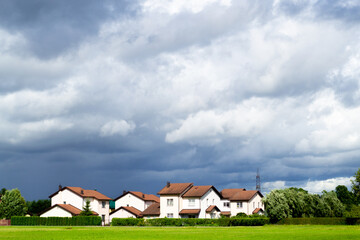 Fototapeta na wymiar A new cottage settlement with a flat green lawn. Nice little houses. Dark gray dramatic clouds. Rainy weather Riga, Latvia