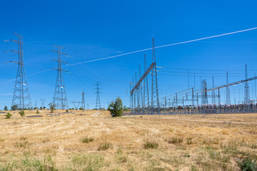 View of high voltage power plant and high voltage cable crossing towers in green grass field