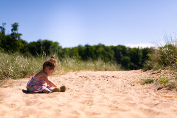 Fototapeta na wymiar A toddler girl sitting in the sand and playing
