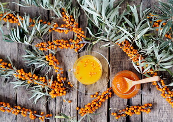 Tea with sea buckthorn jam with branches of fresh sea buckthorn berries on a wooden background....