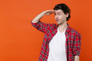 Amazed young brunet man 20s wearing white t-shirt red checkered shirt posing standing holding hand...