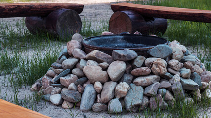 Close-up of a place for a fire pit made of cast iron and stones. Wooden benches near the fire