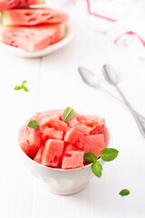 Juicy ripe sweet red watermelon slices with mint leaves in a bowl on a white background, delicious summer berries