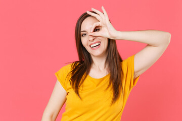 Fototapeta premium Cheerful smiling young brunette woman 20s in yellow casual t-shirt posing showing making stick tongue out sign,&nbsp;fooling around looking camera isolated on pink color wall background studio portrait.