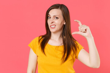 Confused puzzled young brunette woman 20s wearing yellow casual t-shirt posing standing gesturing demonstrating size with workspace looking camera isolated on pink color background studio portrait.