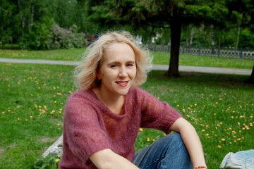 Obraz premium Pretty blond woman sitting on the giant stone ib the park, relaxing after long walk, hard day