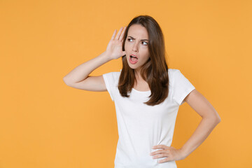 Obraz premium Shocked curious amazed young woman 20s in white blank empty design casual t-shirt posing try to hear you overhear listening intently looking aside isolated on yellow color background studio portrait.