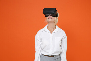Smiling beautiful pretty young blonde female business woman girl 20s wearing white shirt watching in headset posing looking up isolated on bright orange color wall background studio portrait.