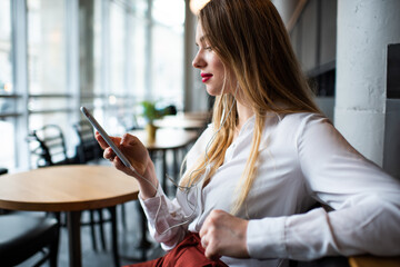 Yong woman in earphones using smartphone in cafe