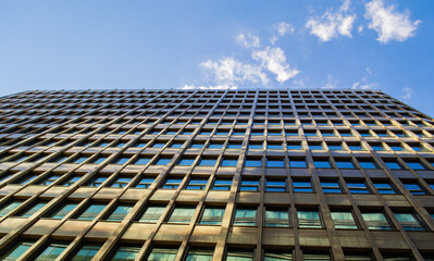 Bottom-up view of a glass modern office building, against a blue sky with clouds