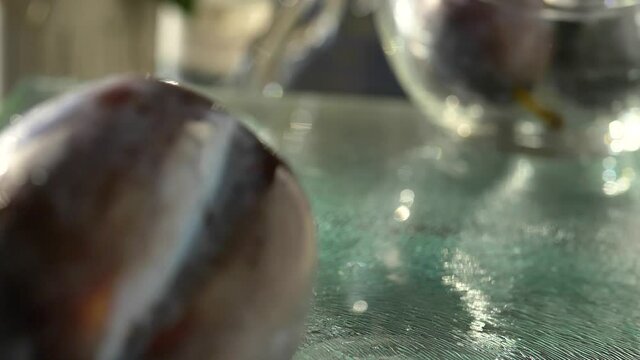 Plums bouncing and rolling on glass cutting board