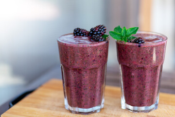 Delicious blackberry smoothie with mint and fresh berries in glasses on wood desk and grey background. Healthy lifestyle concept