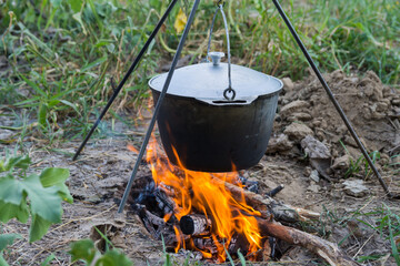 Dinner at the camp. The iron cauldron, blackened by the fire, hangs on a tripod over the fire.