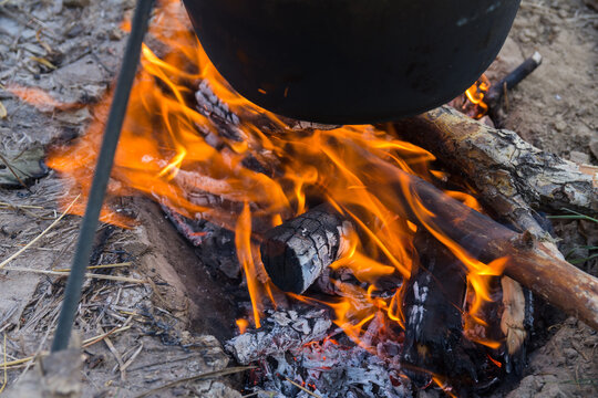 Closeup photo of the bottom of the iron cauldron, blackened by the fire. Cauldron is hanged on a tripod over the fire.