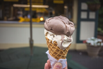 Soft focus of Ice Cream Cone. A hand holding an ice cream cone with scoop of chocolate and vanilla flavor. Blurry ice cream shop background.