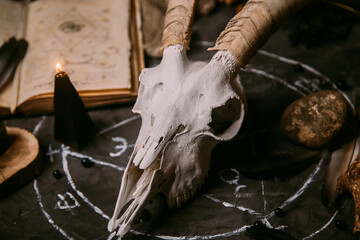 White goat scull with horns, open old book, magic spells, runes, black candles