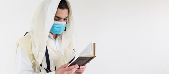 Orthodox Jewish man praying with prayer shawl, tallit, over his head, wearing protective mask against the covid-19 pandemic.