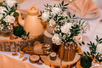 Obraz na płótnie Canvas Wedding decor in rustic style. Wedding table decoration with sawed wood, white roses and green leavers in a bouquet, glass vases , teapot and nuts.
