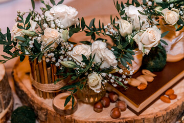Wedding decor  in rustic style.  Wedding table decoration  with sawed wood, white roses and green leavers in a bouquet, glass vases , handmade Eco jars and nuts.