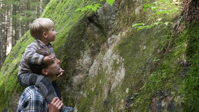 Father and son walking in forest and exploring plants and green moss on rock. Adventure deep in nature, hiking concept, active weekend outdoor, parenting.