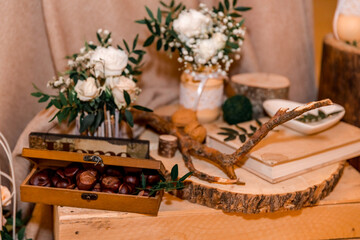 Wedding decor  in rustic style.  Composition on a wooden box of white roses and green leaves in a bouquet, candles, handmade vases, elements of branches, nuts and decorative boxes with nuts.