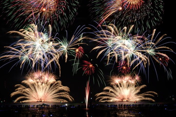 Festive fireworks display light up over night sky at the beach. Colorful firework celebration on dark background.
