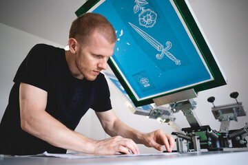 Selective focus of craftsman working on screen printing press in workshop 