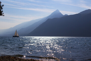 sailing boat on blue water with sun reflection with panoramic view of apls mountain lake