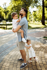 Caring dad with little kids at the park, lovely man hold in arms cute son, smiling, beautiful daughter hug loving father, enjoy tender family moments, parenthood concept