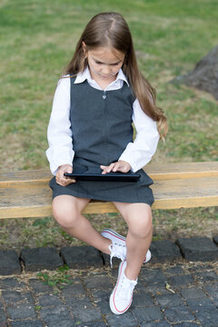 Little child in school uniform touch screen or touchscreen finger push tablet computer icon sitting on bench outdoors, e-school