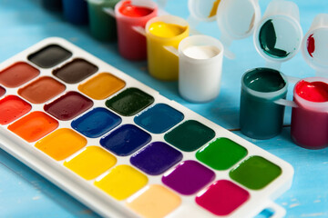 Colorful jars with gouache and watercolors on a blue background.