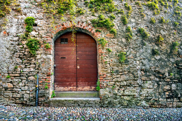 Street view with wooden outdoor door on medieval stone wall in Bergamo. Lombardy, Italy