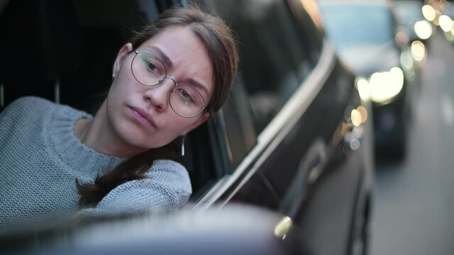 Close-up of a young woman looking through a car window in a traffic jam in the evening. rush hour