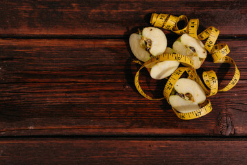 A delicious and healthy snack for healthy and active people. Small pieces of sliced fresh Apple lie on the mahogany kitchen table, and a yellow fitness measuring tape is next to it.