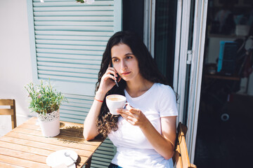 Young woman speaking on smartphone and drinking coffee in outdoor cafe