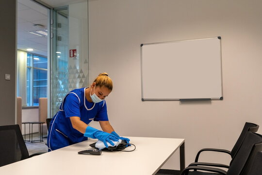 A cleaning lady with a mask on her face cleans the meeting room.