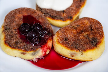 Homemade cheesecakes on a white plate with cherry jam and sour cream.  close-up photo