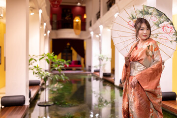 Young woman wearing a kimono, Japanese culture with an umbrella,  looking at the camera. Japanese concept of kimono and yukata.