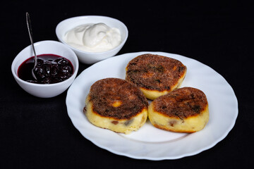 Homemade cheesecakes on a white plate with cherry jam and sour cream.  close-up photo on a black background.