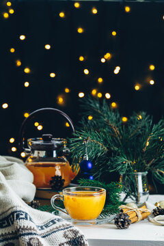 Christmas and New Year composition. Cup and teapot of hot spicy tea with sea buckthorn, jam in the glass jar, branches of pine and spruce, holiday decor, bokeh