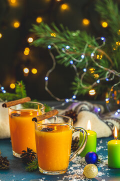Christmas and New Year composition. Two cup of hot spicy tea with sea buckthorn, cinnamon and star anise, branches of pine and spruce, candles and holiday decor, bokeh