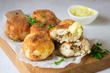 Classic homemade Italian arancini. Fried rice balls with minced meat served with parsley and cheese sauce. Light stone background.