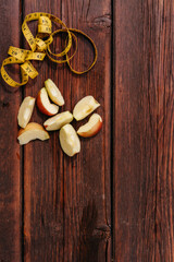 A delicious and healthy snack for healthy and active people. Small pieces of sliced fresh Apple lie on the mahogany kitchen table, and a yellow fitness measuring tape is next to it.