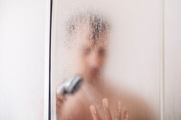 Man taking a shower washing hair with shampoo product under water falling from luxury rain shower head.