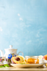 Fresh homemade peach jam in glass jar on a wooden background. Several fresh berries, mint and all for tea party are near it.
