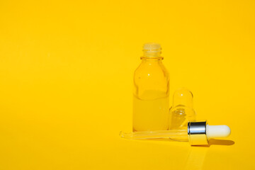 Yellow serum liquid oil in clear bottle with dropper on orange background. Organic SPA cosmetics with herbal ingredients. Citrus essential oil, cosmetics aromatherapy. Flat lay. Copy space.