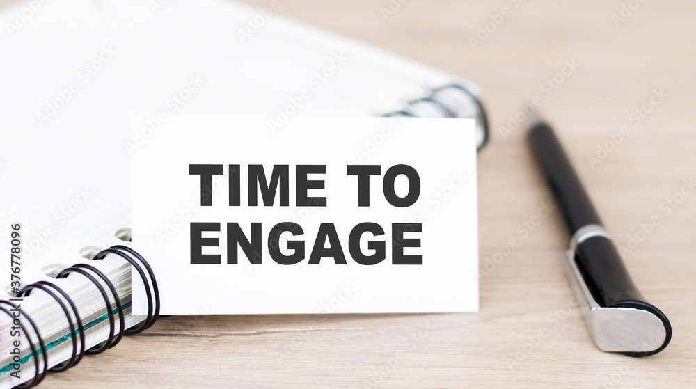 Aufkleber white card on with text time to engage on the background of a notebook and pen
