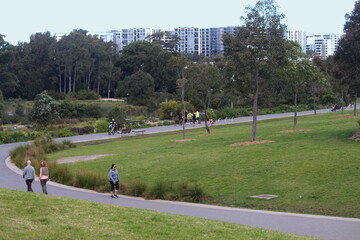 Sydney, NSW / Australia - August 23 2020: People walking along a meandering path at Sydney Park with trees and apartment buildings in the background
