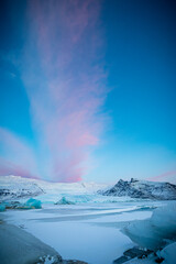 Pink clouds rise above ice at dawn  in Jokulsaralon in Iceland.